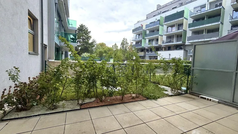 Geräumige Terrasse mit Fliesenboden und kleinen Sträuchern, umgeben von modernen Wohngebäuden.