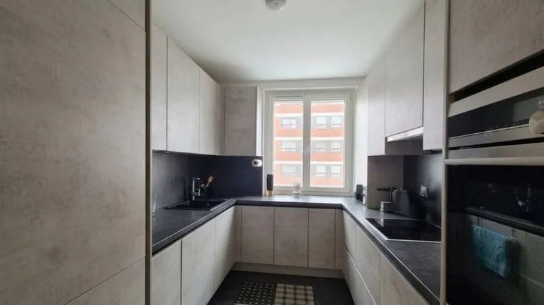 Moderne Küche mit hellgrauen Schränken, dunkler Arbeitsplatte und Fensterblick auf Gebäude.