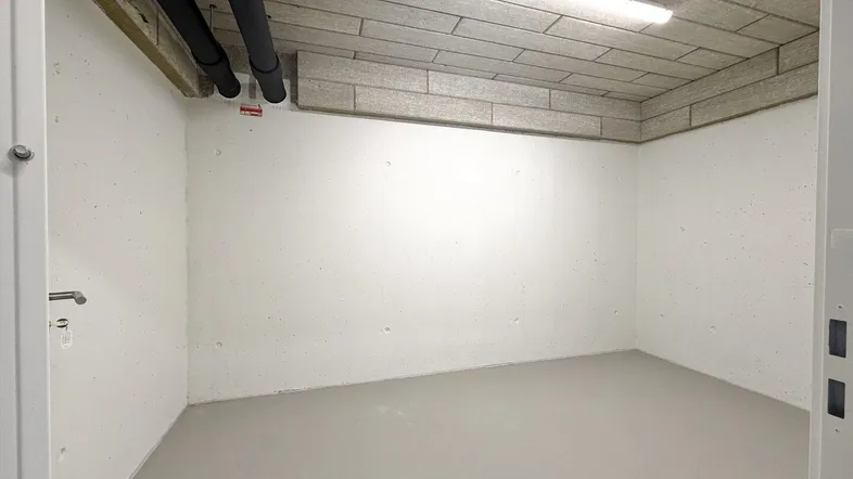 Leerer Lagerraum mit Betonboden und sichtbaren Rohren sowie Leitungen an der Decke.