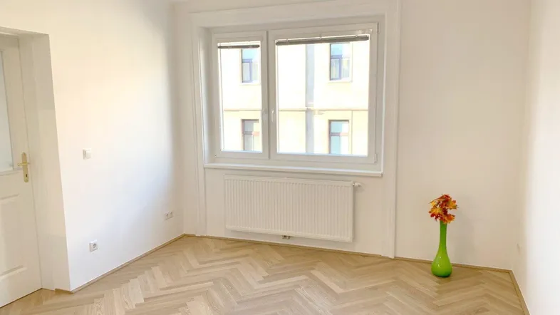 Helles Zimmer mit Fischgrätparkett und Blick auf die gegenüberliegende Bebauung.
