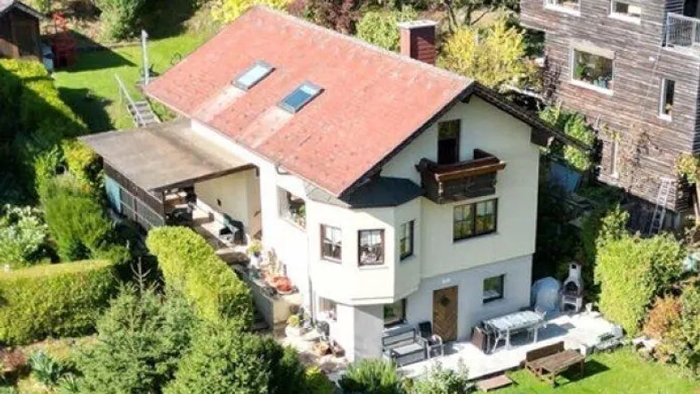 Luftaufnahme eines charmanten Hauses mit rotem Ziegeldach, umgeben von einem grünen Garten und Bäumen.