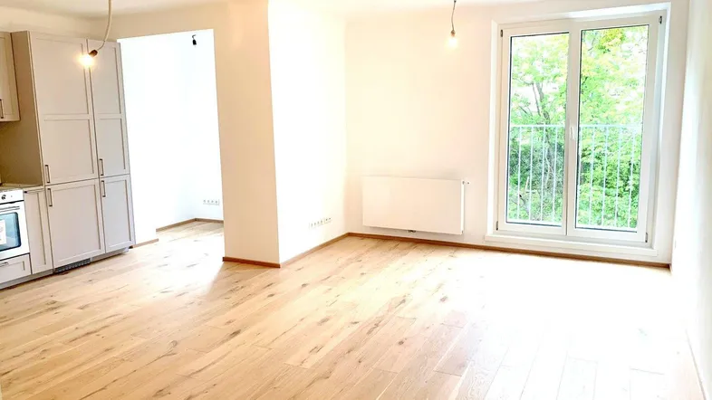 Helles, offenes Wohnzimmer mit Parkettboden, integrierter Küche und Zugang zum Balkon.