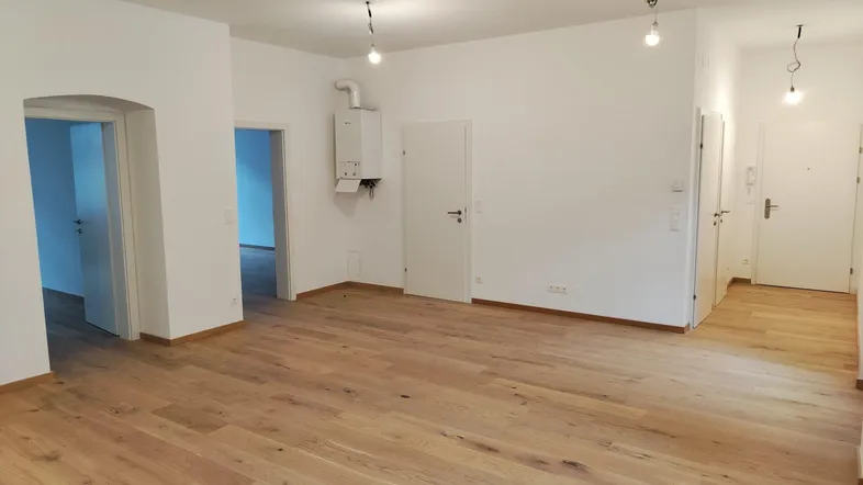 Heller, unmöblierter Wohnbereich mit neuem Holzparkettboden und Zugang zu weiteren Räumen.