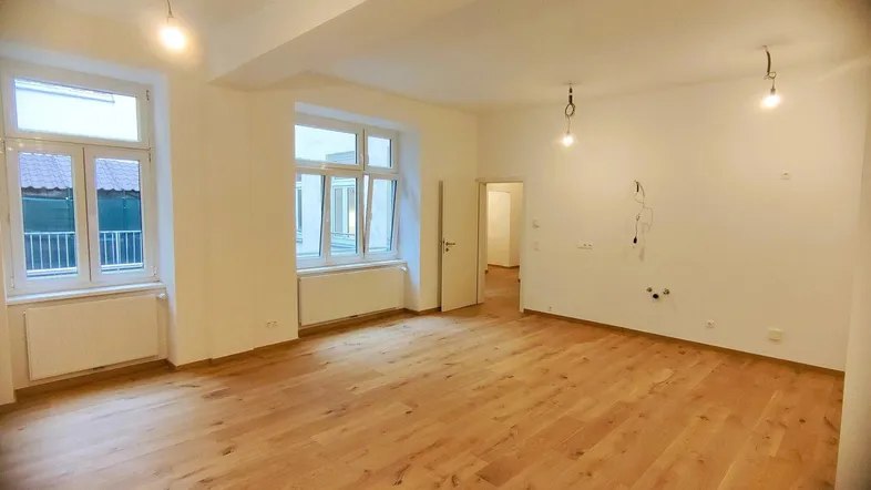 Helles, leeres Zimmer mit neuem Holzfußboden und großen Fenstern, bereit zur individuellen Gestaltung.