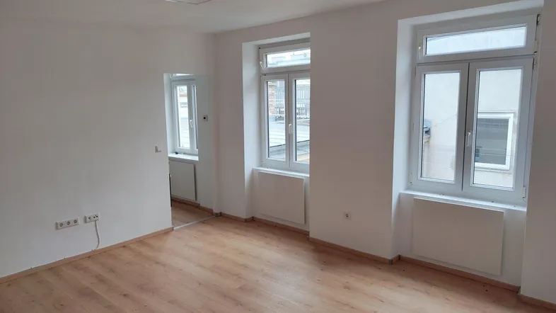 Helles Zimmer mit Laminatboden und zwei Fenstern, bereit zur individuellen Gestaltung.