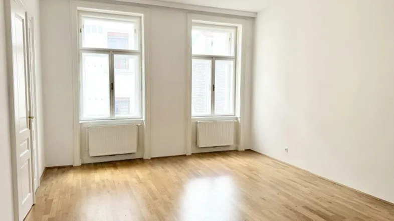 Helles Zimmer mit Parkettboden, weißen Wänden und zwei großen Fenstern, bereit zum Einzug.