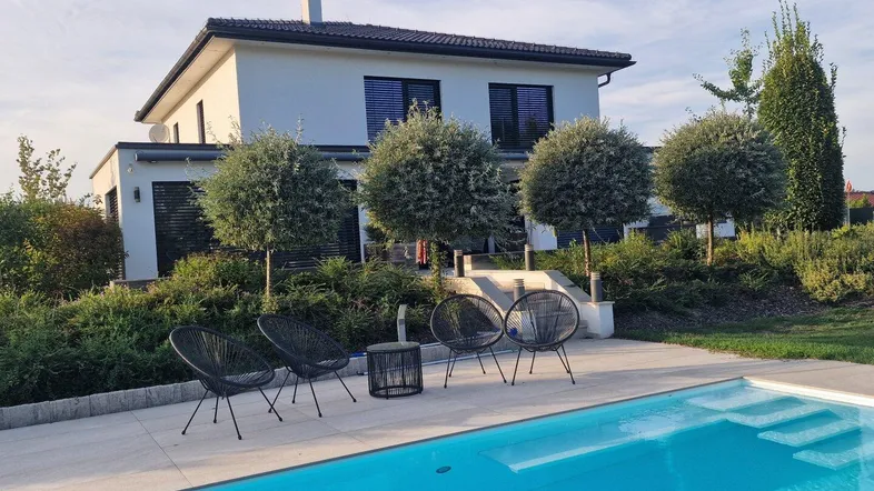 Modernes Haus mit Swimmingpool, Liegefläche und Gartenmöbeln im Außenbereich.