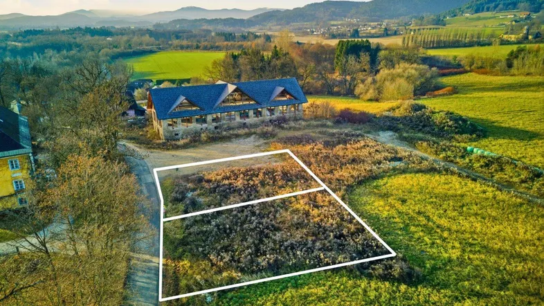 Luftaufnahme eines Baugrundstücks mit markierten Grenzen in ländlicher Umgebung und Bergen im Hintergrund.