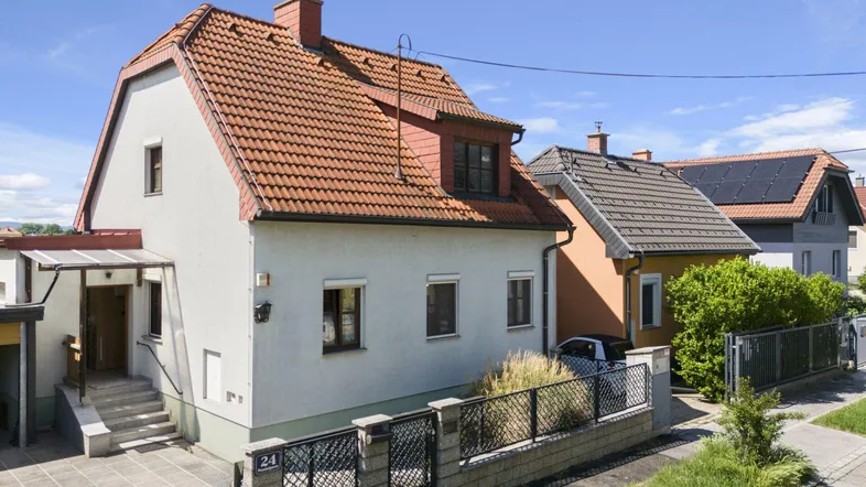 Vorderansicht eines Einfamilienhauses mit Satteldach, Vorgarten und gepflegter Fassade unter blauem Himmel.