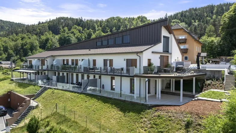 Modernes Mehrfamilienhaus mit mehreren Balkonen und Terrassen in grüner Hanglage.