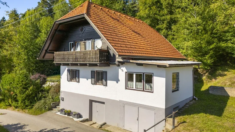 Freistehendes Haus mit Satteldach, Balkon und integrierter Garage, umgeben von viel Grün.