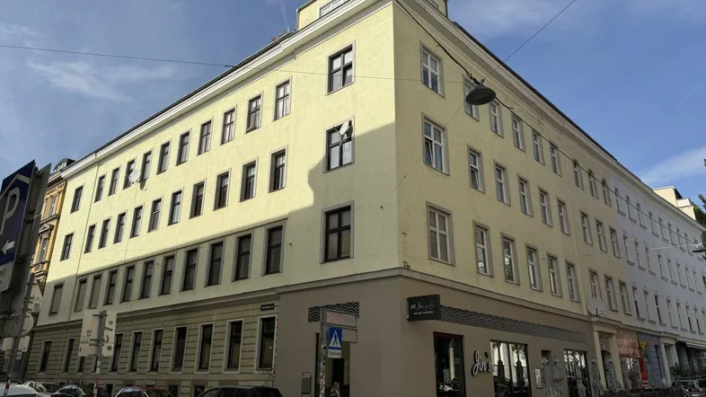 Gelbes Eckgebäude mit vielen Fenstern und Geschäften im Erdgeschoss an einer städtischen Straße.