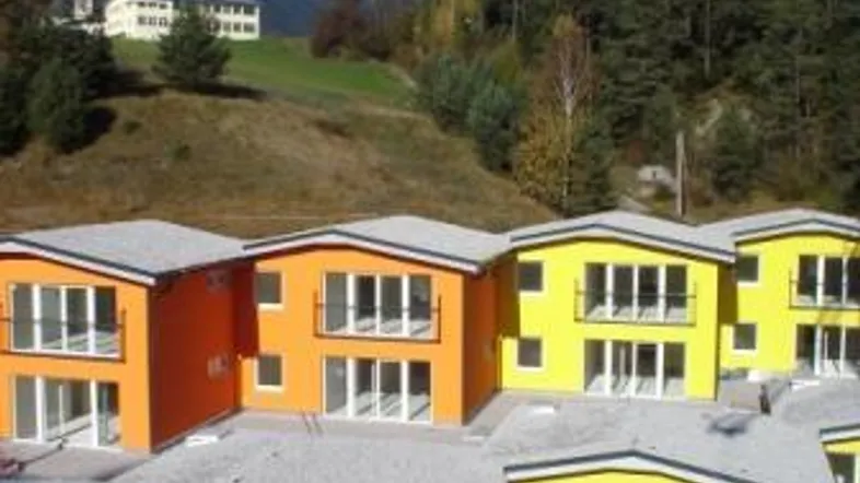 Reihenhäuser in leuchtenden Farben mit Blick auf die umliegende Berglandschaft und grüne Hügel.