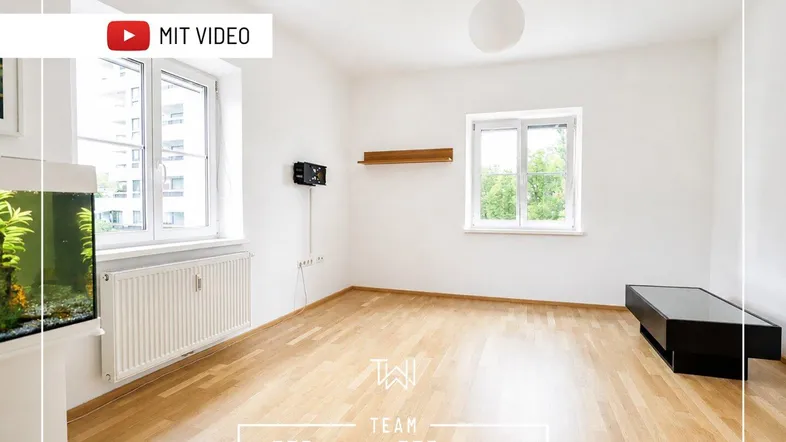 Heller Wohnraum mit Parkettboden, weißen Wänden und Blick ins Grüne durch die Fenster.