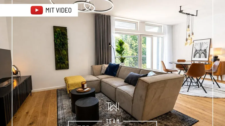 Heller, offener Wohn- und Essbereich mit modernem Sofa, Holzboden und großen Fenstern mit Blick ins Grüne.