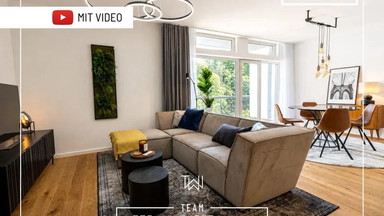 Moderner offener Wohn- und Essbereich mit beigem Sofa, Holzboden und großen Fenstern mit Blick ins Grüne.
