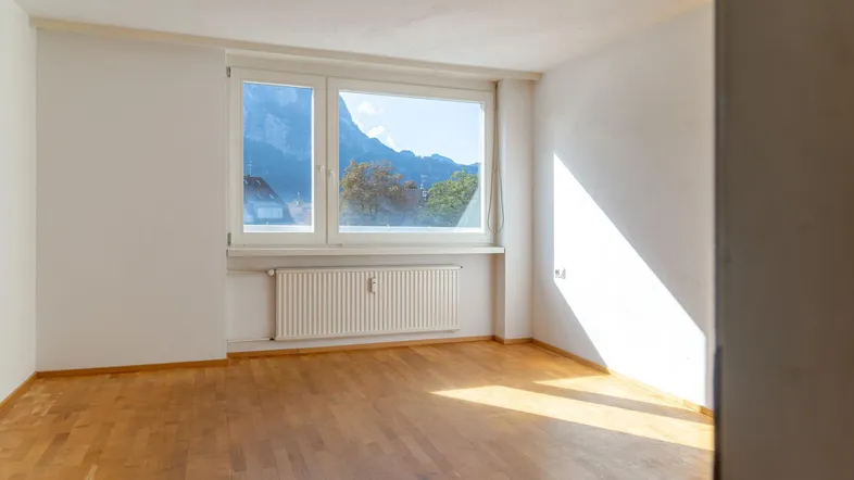 Helles Zimmer mit Parkettboden, weißen Wänden und einem schönen Bergblick durch das Fenster.