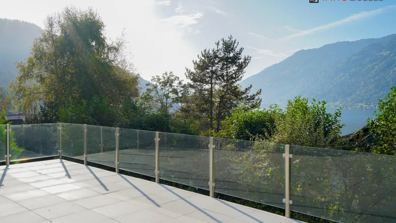 Große geflieste Terrasse mit Glasgeländer und herrlichem Blick auf die Berge und den See.