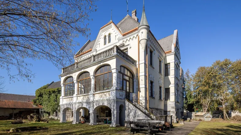 Historische Villa mit markanter Architektur, Türmchen und großzügiger Veranda in ländlicher Umgebung.