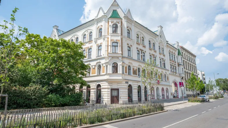 Historisches Eckgebäude mit markanter Architektur und vielen Fenstern an einer belebten Straße.