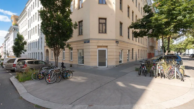 Eckgebäude mit heller Fassade und Fahrrädern auf dem Bürgersteig in einer städtischen Umgebung.