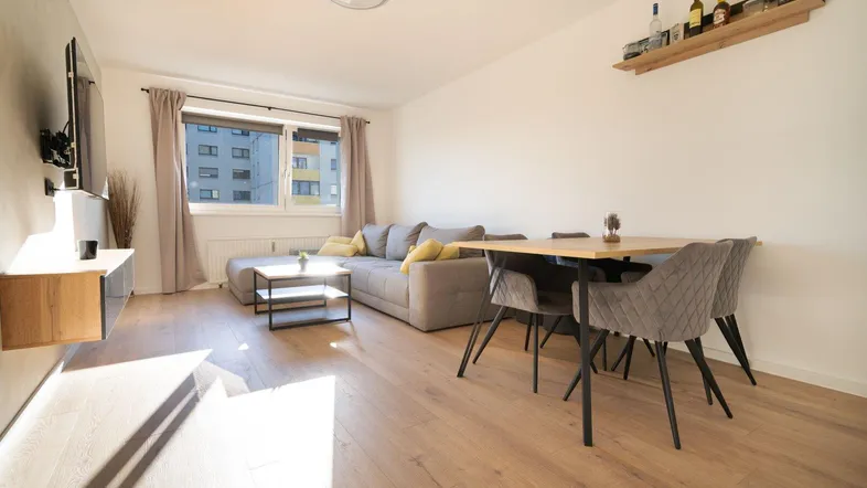 Helles Wohn- und Esszimmer mit modernem Laminatboden, bequemer Couch und Esstisch für vier Personen.