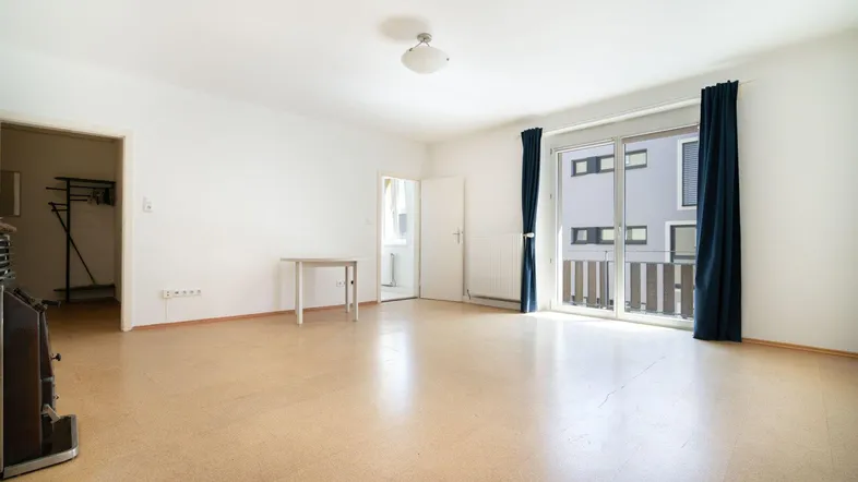Helles Wohnzimmer mit Parkettboden, Kachelofen und Zugang zum Balkon.