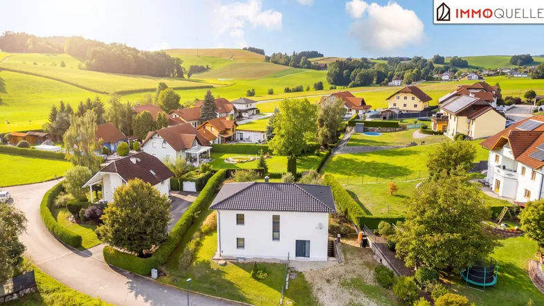 Luftaufnahme einer Wohnsiedlung mit Einfamilienhäusern und grüner Hügellandschaft im Hintergrund.