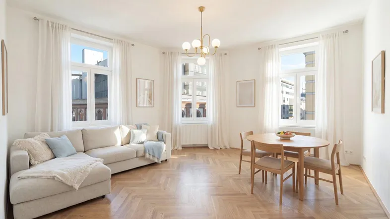 Helles Wohn- und Esszimmer mit Fischgrätparkett, beigem Sofa und modernem Esstisch.