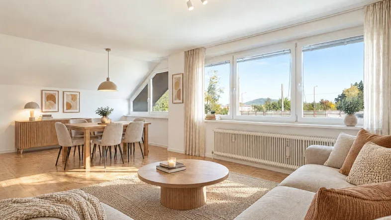 Helles, modern eingerichtetes Wohn-Esszimmer mit großen Fenstern und Blick ins Grüne.