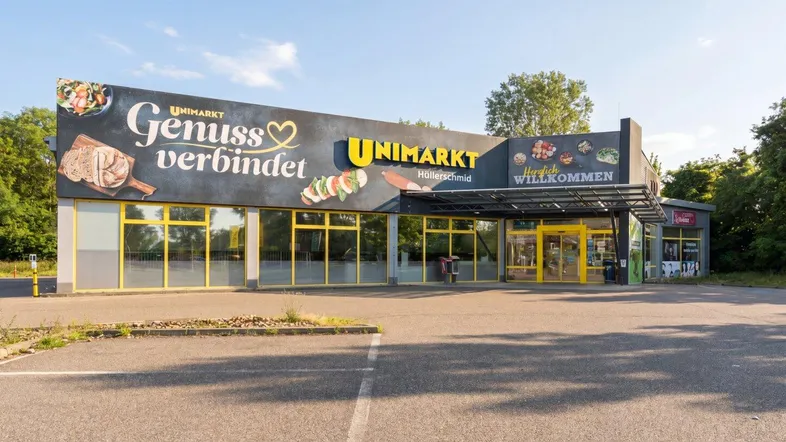 Außenansicht eines Supermarktes mit großflächiger Beschilderung und einem geräumigen Parkplatz davor.