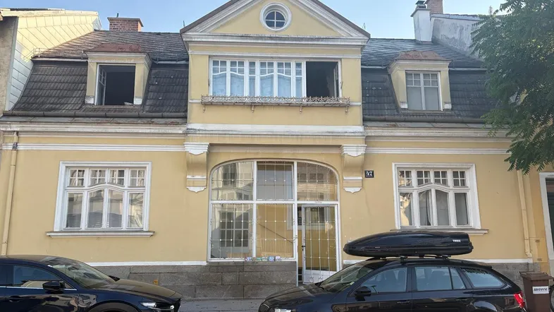 Gelbe Fassade eines Altbaus mit mehreren Fenstern und parkenden Autos davor.