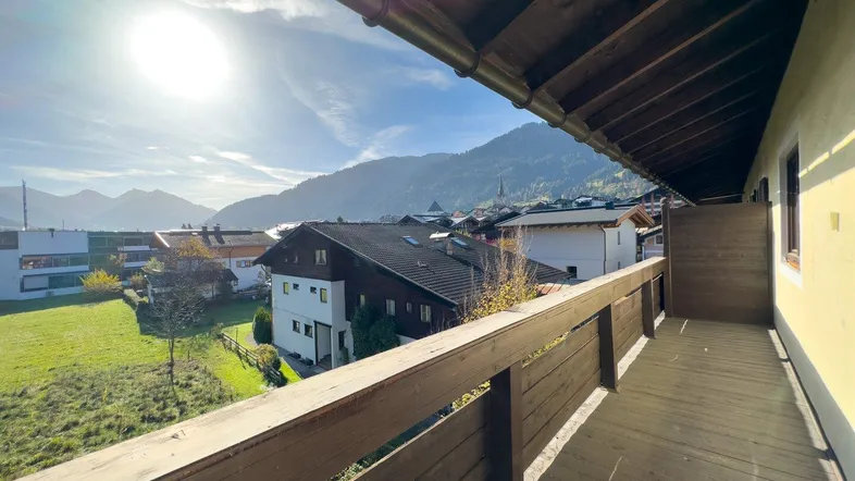 Sonniger Balkon mit Holzboden und Geländer, bietet einen weiten Blick auf die umliegende Berglandschaft.