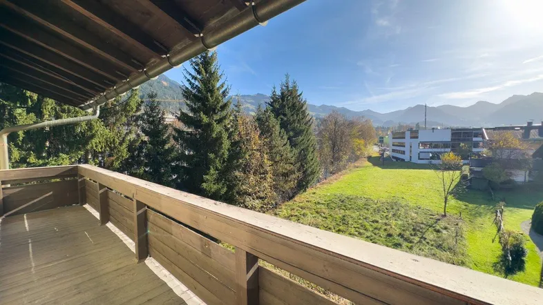 Geräumiger Balkon mit Holzboden und weitem Blick auf grüne Wiesen und bewaldete Berge.