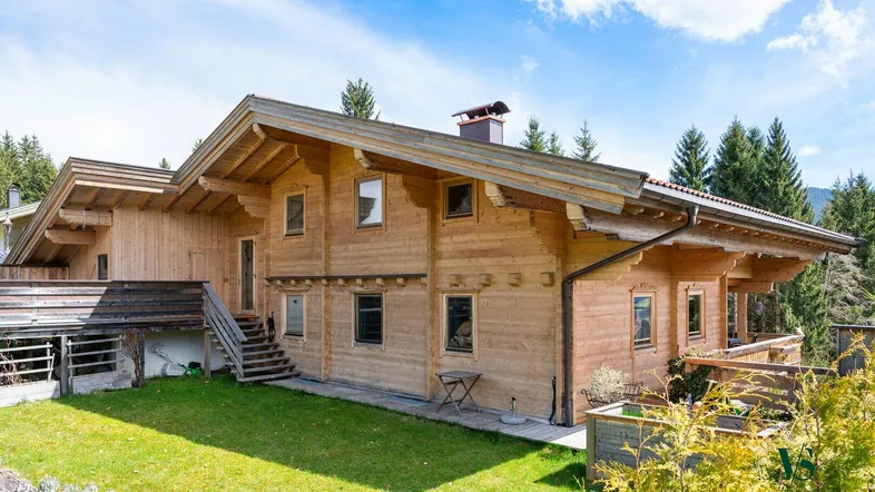 Traditionelles Holzhaus im alpinen Stil mit gepflegtem Rasen und umgebender Natur unter blauem Himmel.