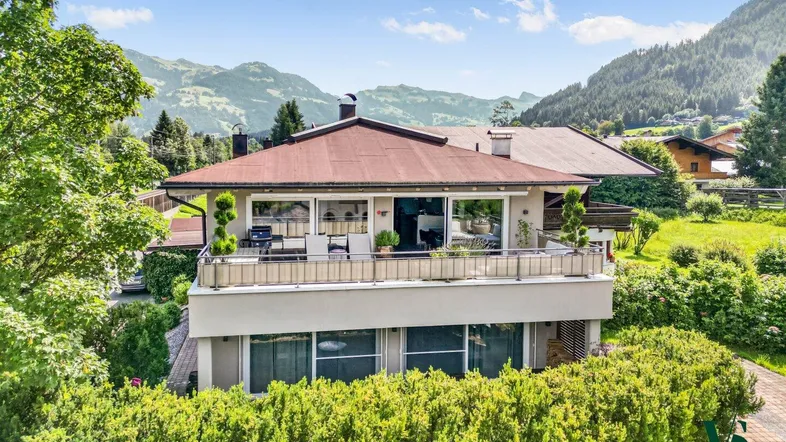 Geräumiges Haus mit großem Balkon und atemberaubendem Bergblick, umgeben von üppigem Grün.