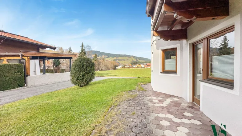 Gepflasterter Außenbereich neben dem Gebäude mit Rasenfläche und Blick auf die umliegende Landschaft.