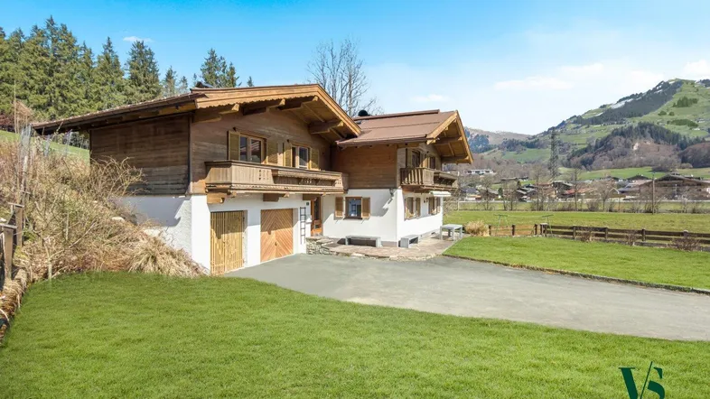 Traditionelles Holzhaus im alpinen Stil mit gepflegtem Rasen und Bergblick unter blauem Himmel.