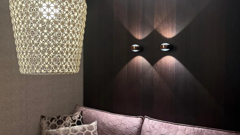 Gemütliches Wohnzimmer mit lila Sofa, dekorativer Hängelampe und dunkler Holzvertäfelung an der Wand.