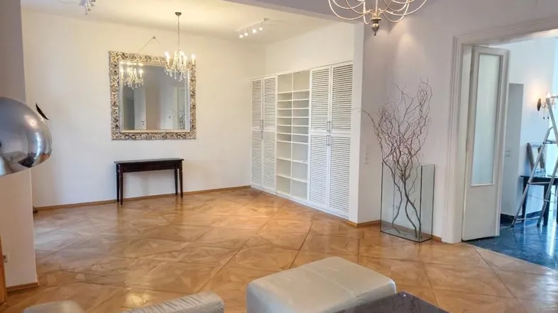 Geräumiges Wohnzimmer mit elegantem Parkettboden, großem Spiegel und integrierten Schränken.