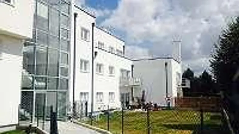 Modernes weißes Gebäude mit Glasfassadenaufzug und gepflegter Rasenfläche im Außenbereich.