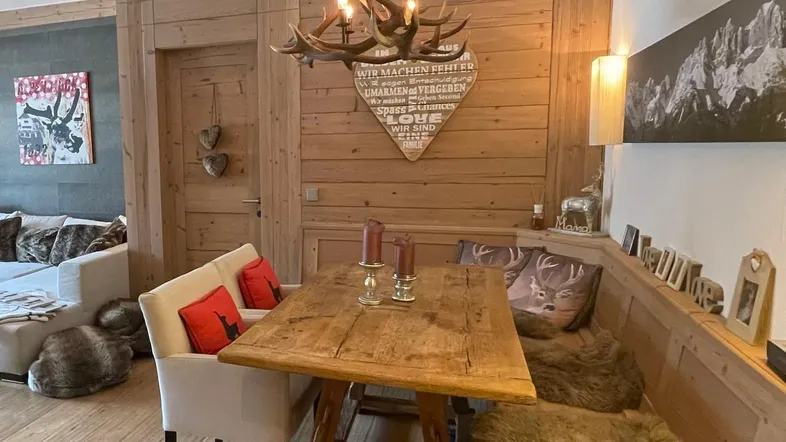 Gemütlicher Essbereich im alpinen Stil mit Holztisch, Eckbank und Hirschgeweih-Kronleuchter.