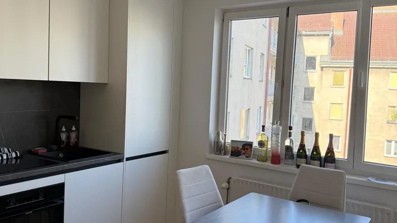 Moderne Küche mit weißen Schränken, dunkler Arbeitsplatte und Essbereich am Fenster mit Stadtblick.