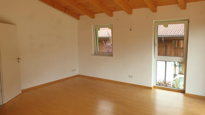 Helles Zimmer mit Holzbalkendecke, Parkettboden und zwei Fenstern für viel Tageslicht.