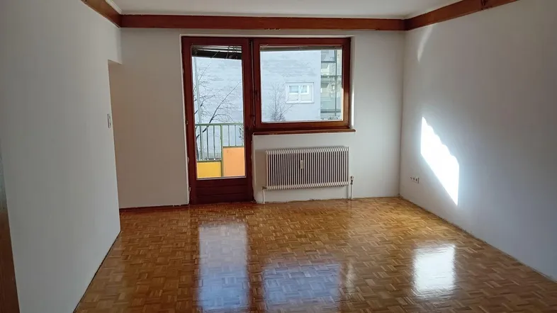 Helles Zimmer mit Parkettboden, Holzbalkendecke und Zugang zu einem Balkon.