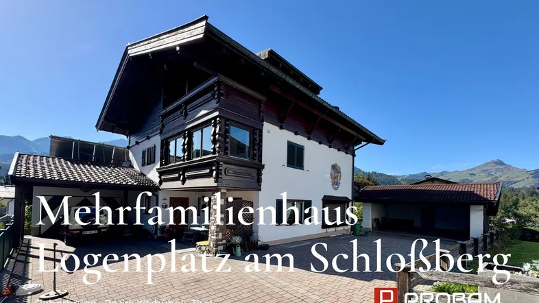 Mehrfamilienhaus im alpinen Stil mit traditionellen Holzelementen und Bergblick unter blauem Himmel.