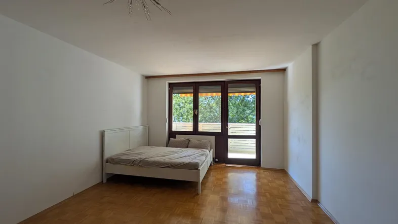 Helles Schlafzimmer mit Parkettboden, einem Bett und Zugang zu einem Balkon oder einer Terrasse.
