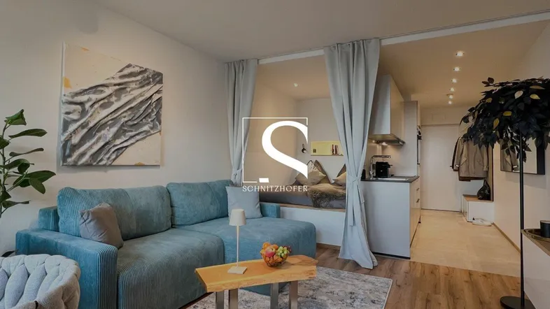 Modernes Wohnzimmer mit bequemer Couch, Holzboden und integrierter Küchenzeile.