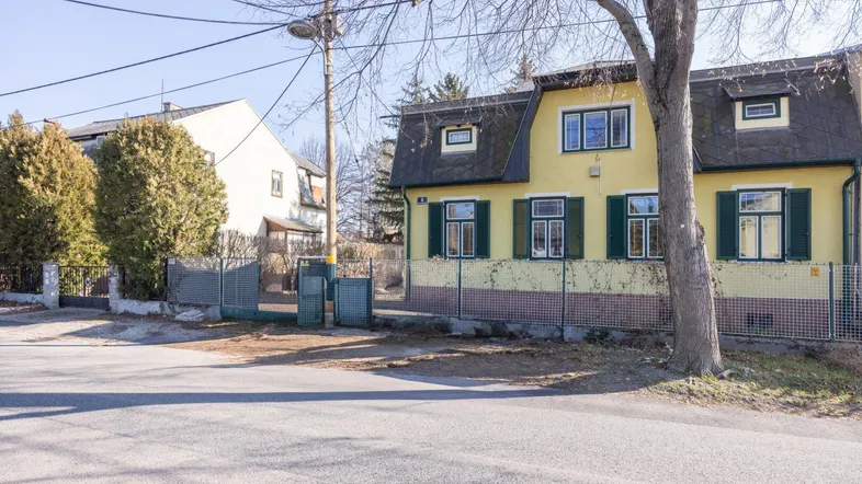 Gelbes Haus mit grünen Fensterläden und Mansarddach von der Straße aus gesehen.