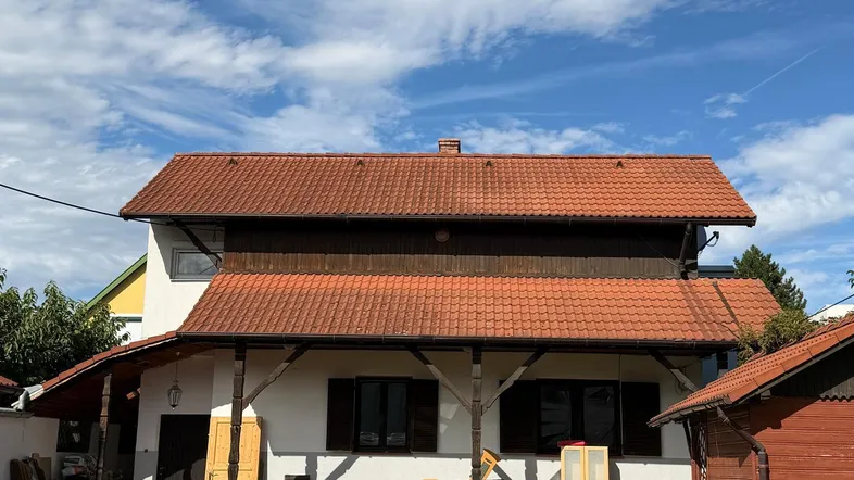 Weißes Haus mit rotem Ziegeldach, überdachtem Eingangsbereich und Rasenfläche unter blauem Himmel.